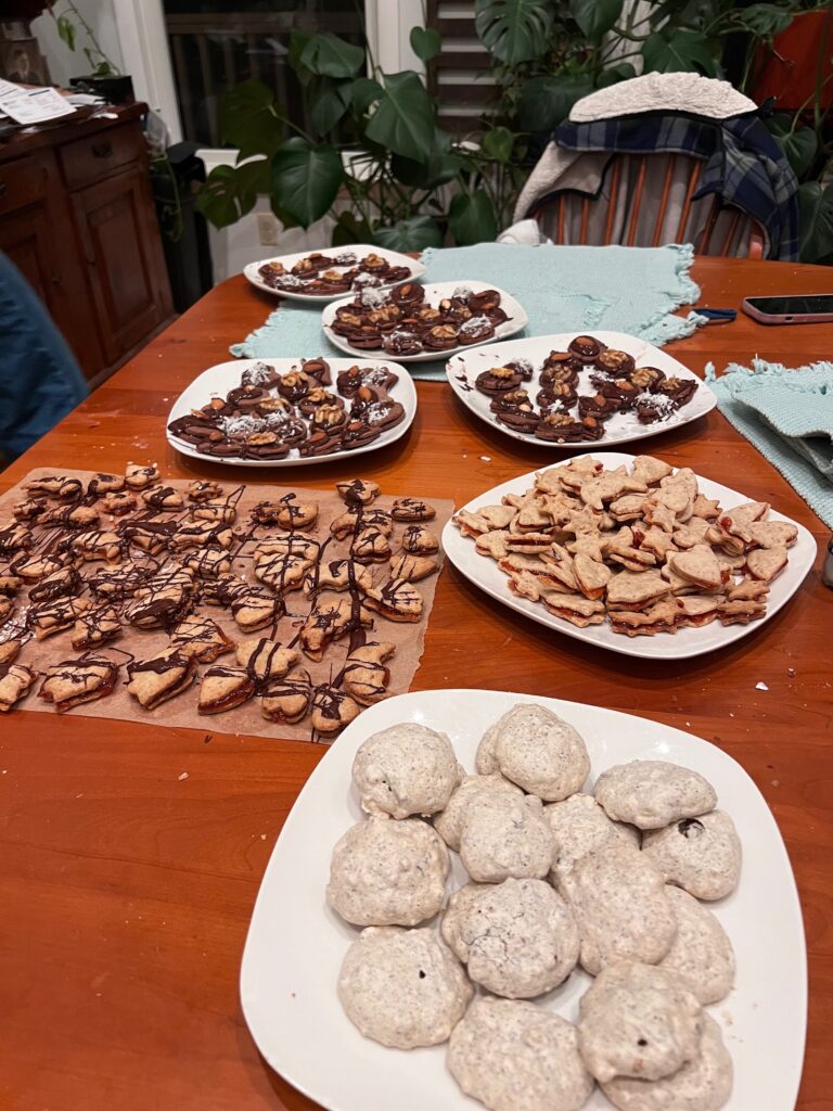 A dining room table is covered with six plates of holiday cookies.