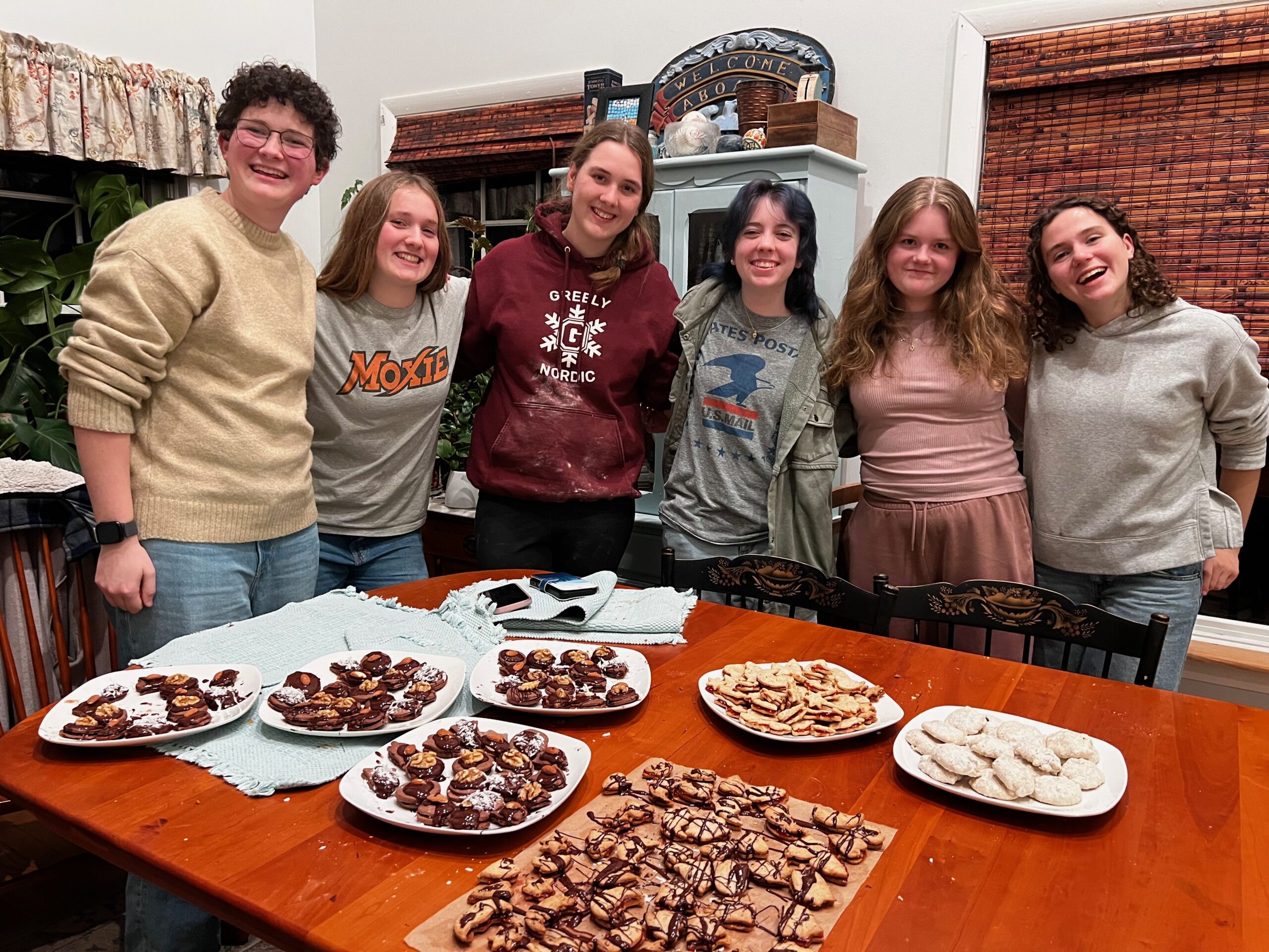 A group of six high school students pose for a picture behind a dining room table with the holiday cookies they made.