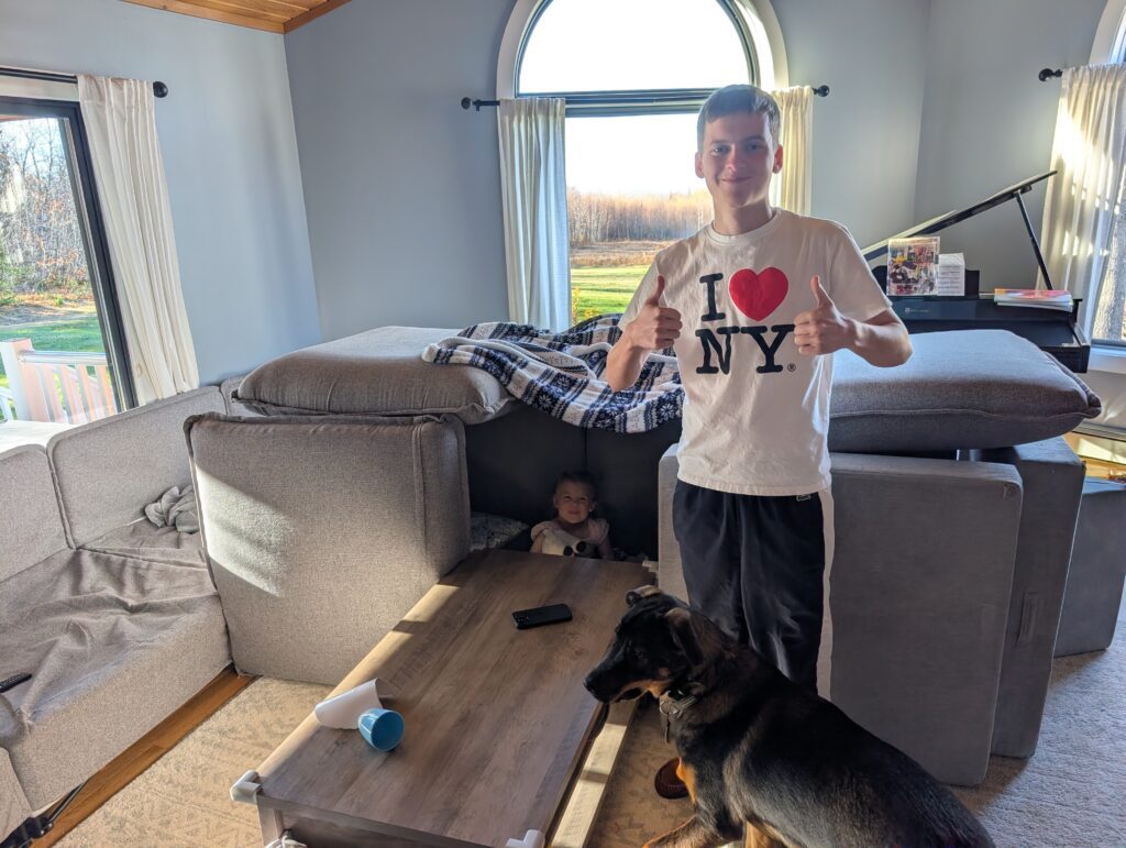 Max poses with his thumbs up, in front of the couch-and-pillow fort he made with his host sister, Sophia.